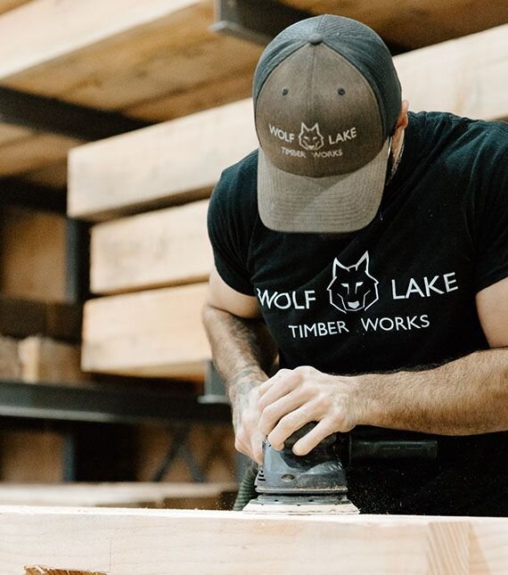 A craftsman sanding wood for a timber frame structure, emphasizing craftsmanship and quality